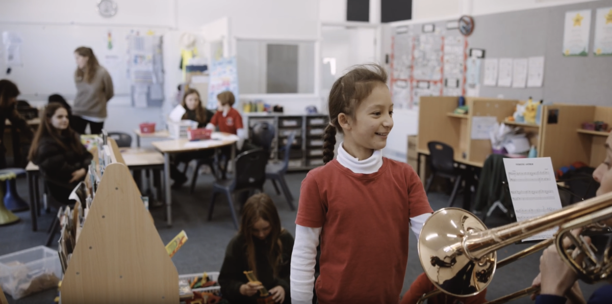 Young girl interacts with a musician playing a brass instrument in a classroom